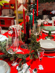 Christmas set table is adorned with festive decorations, ready for a joyful winter holiday gathering. Vibrant red tablecloth and elegant tableware create a warm and inviting atmosphere