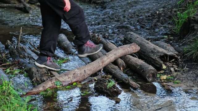 Kid in Trekking Shoes Crossing Shallow Water Forest Creek Water Stream Footbridge Made with Chopped Tree Logs