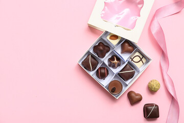 Box with delicious chocolate candies and ribbon on pink background