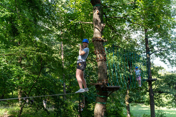 Woman in helmet walking on rope bridge during obstacle course in the forest, balancing. Concept of...