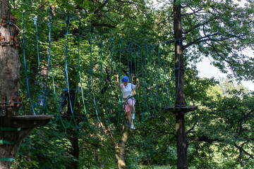 Young woman crossing a high rope obstacle course in the forest. Concept of outdoor adventure,...