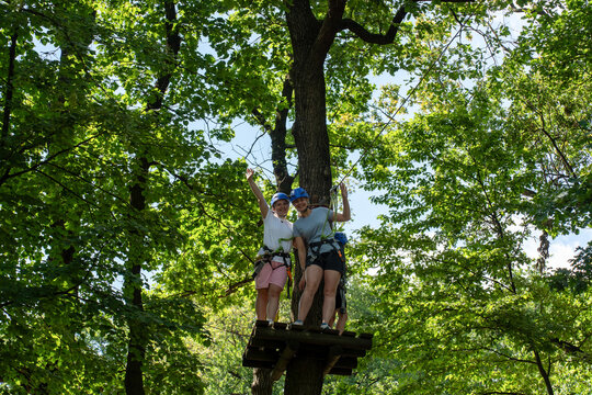 Two women in helmets enjoying rope course on a platform high in the trees during a sunny day. Concept of outdoor adventure, team bonding, and active lifestyle in nature. High quality photo