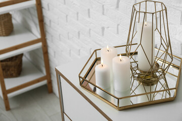 Burning candles on dresser near white brick wall in living room, closeup
