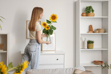 Beautiful young happy woman holding vases with sunflowers bouquets at home