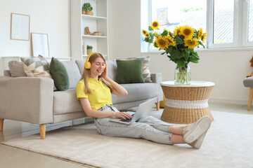 Beautiful young happy woman in headphones with laptop and bouquets of sunflowers sitting at home