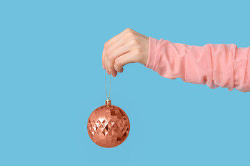 Female hand with Christmas ball against color background, closeup
