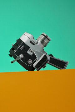 Retro Vintage Tech 8mm Film Movie Camera still life on edge of orange surface with teal mint green background, old school summertime vibes.