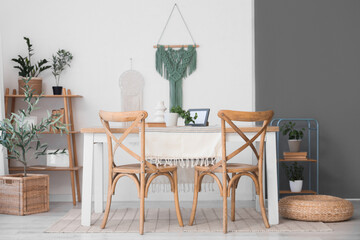 Interior of light dining room with table, pouf and chairs near white wall