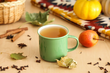 Autumn leaves, cup of hot green tea, apple and scattered spices on table in kitchen, closeup