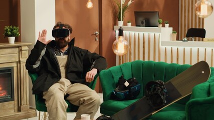 Person uses virtual reality headset in lounge area, having fun with vr innovative glasses while he wears winter attire. Tourist having helmet and snowboard, prepare to go sliding. Tripod shot.