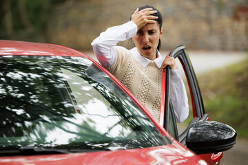 Woman with her hands on her head upset because her car broke down in the middle of the road on her...