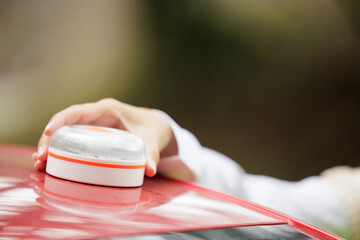 Young woman with reflective vest, places the V16 emergency light beacon on the roof of the damaged vehicle. Help flash, mandatory to replace triangles in Europe. DGT Spain.