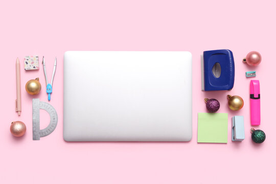 Laptop with stationery supplies and Christmas balls on pink background