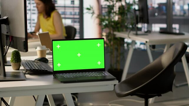 Green screen laptop on desk in workspace with admins in background doing software quality assurance. Chroma key notebook in office with woman at work inspecting coding on device, camera A