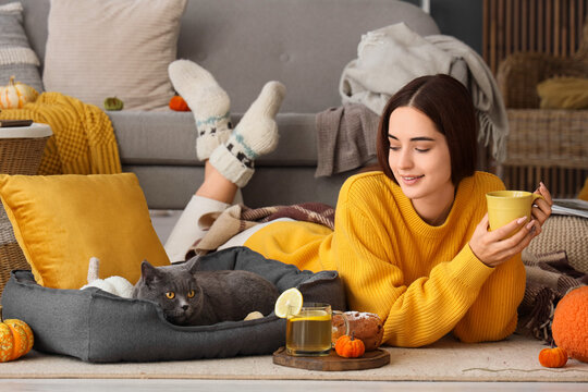 Young woman with cup of tea and cute British cat lying at home on autumn day