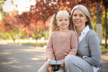 Cute little girl with photo camera and her mother in park on autumn day
