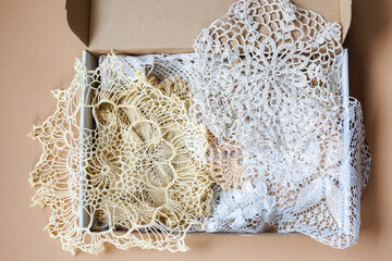 A large number of lace handmade crocheted doilies in a cardboard box on a brown background....