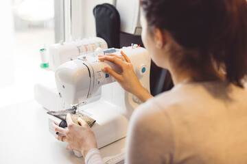 Unrecognizable woman sewing on a sewing machine. Woman learning how to use a sewing machine at home in her free time.