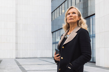 A female leader walks in front of an office building in cloudy weather. She meets a male businessman. They are discussing a new deal. They are dressed in business clothes.