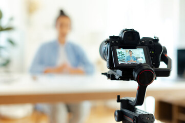 On a camera screen pretty indian or arabian brunette young woman, blogger, influencer sits at a desk, looking at camera, recording education tutorial vlog, video course for social media