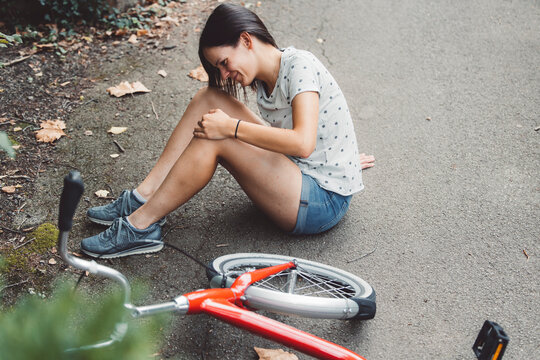 Young caucasian woman riding a red bicycle, captured moments before and after an accident outdoors. Accident with a bike, hurt her knee after she fell on the road on the way home.