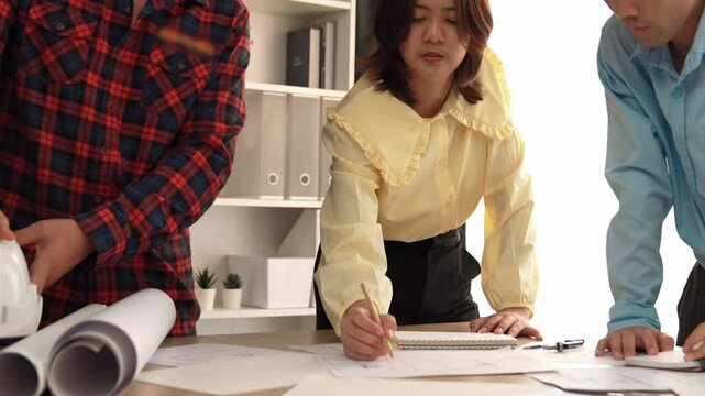 Smart architect and safety engineer discussion about building blueprint on table with architectural document, measurement tools and wooden block scatter around at modern office. Closeup. Delineation.