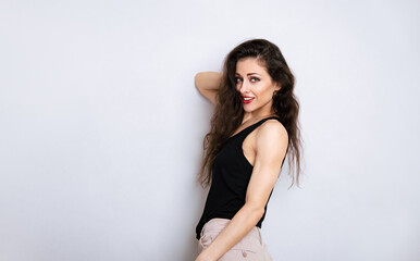 Happy toothy smiling make-up woman with red lipstick, long brown hair looking happy in black top on empty copy space studio blue background. Portrait front view