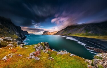 Naklejka premium A stunning view of a rugged coastline with a black sand beach and turquoise water. The dramatic sky is filled with dramatic clouds.