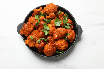 Baked cauliflower buffalo wings with parsley in baking dish on white marble table, top view