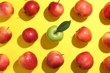 Flat lay composition with green apple surrounded by red ones on yellow background