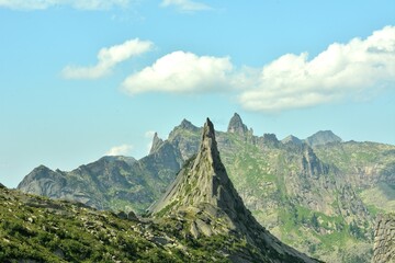 A high elongated rock with a steep slope and a pointed peak in a mountain system under a cloudy...