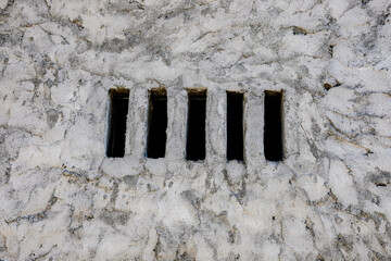Close-up of a textured stone wall with vertical slits, creating a unique architectural detail that combines rustic and minimalist elements, perfect for backgrounds or design use