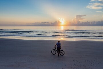 Fototapeta premium Man on a bicycle on a beach looking out to the sunrise, Daytona Beach, Florida, United States.