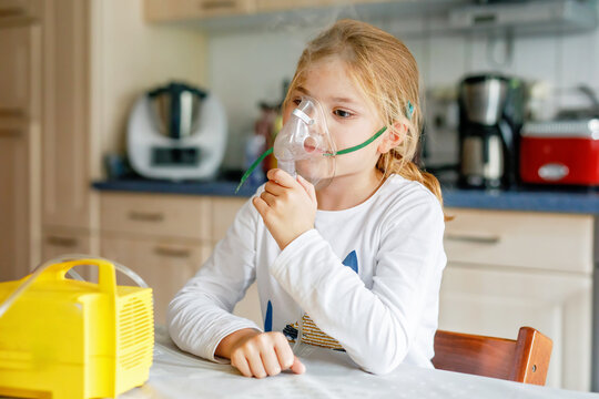 Cute little school girl sitting and holding a nebulizer mask leaning against the face, airway treatment concept. Treatment against caugh. Child smiling