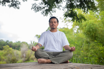 Fototapeta premium A man is sitting on a wooden platform in a forest, meditating