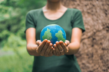 An Asian woman holds a globe in a green forest,symbolizing the importance of preserving...