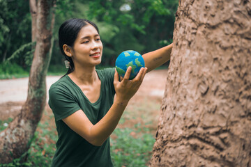 An Asian woman holds a globe in a green forest,symbolizing the importance of preserving...