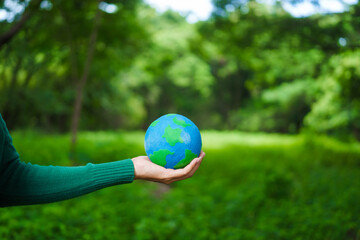 An Asian woman holds a globe in a green forest,symbolizing the importance of preserving...