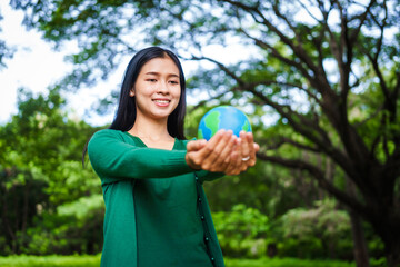 An Asian woman holds a globe in a green forest,symbolizing the importance of preserving...