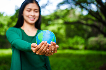 An Asian woman holds a globe in a green forest,symbolizing the importance of preserving...