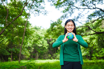 An Asian woman holds a globe in a green forest,symbolizing the importance of preserving...