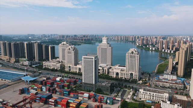 Aerial view of tall buildings and a cluster of shipping containers by the riverside.