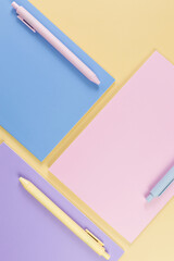 Top view of pink, purple and blue notebooks on yellow background. Pink, yellow and blue pens, school, office wallpaper. Flat lay, copy space.