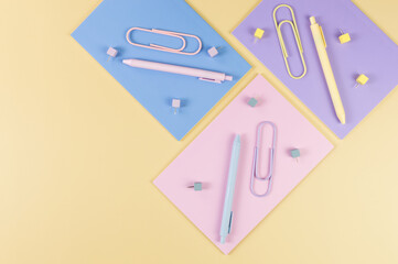 Top view of pink, purple and blue notebooks on yellow background. Colorful pens, paperclips, pins, school, office wallpaper. Flat lay, copy space.