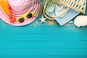 Summer bag with flip flops, towels, hat, seashells and sunglasses on blue wooden table