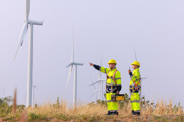 young male and female engineers wearing uniform and hardhats walking together, checking wind...