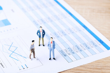 Miniature people and financial papers with graph and charts
