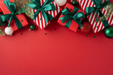 Red and white Christmas gifts with green bows and festive decor arranged on a vibrant red...