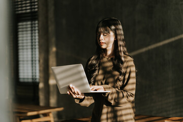 Focused on the Task: Woman Working on Laptop in Sunlight Streaks  