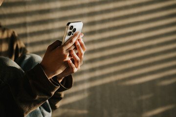 Golden Hour Smartphone: Close-up of hands using a smartphone, bathed in warm sunlight streaming through blinds.  A tranquil and evocative image perfect for illustrating connection, technology.